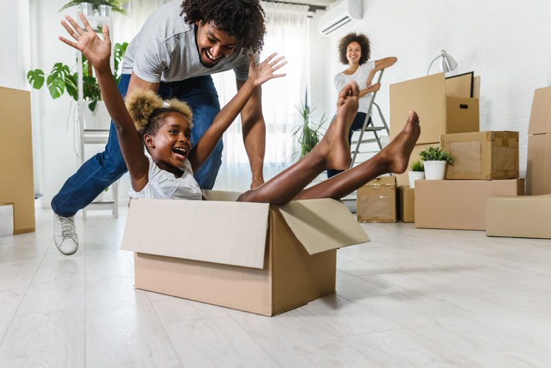 Family enjoys moving day; child plays in cardboard box.