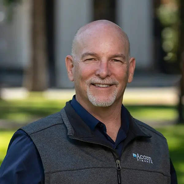 Bearded man outdoors, smiling in vest with Chuck Horton logo.
