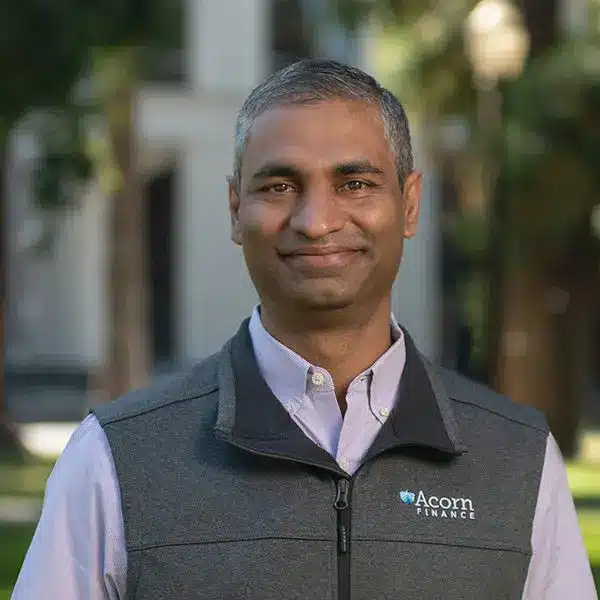 Smiling man outdoors in vest with acorn finance logo.
