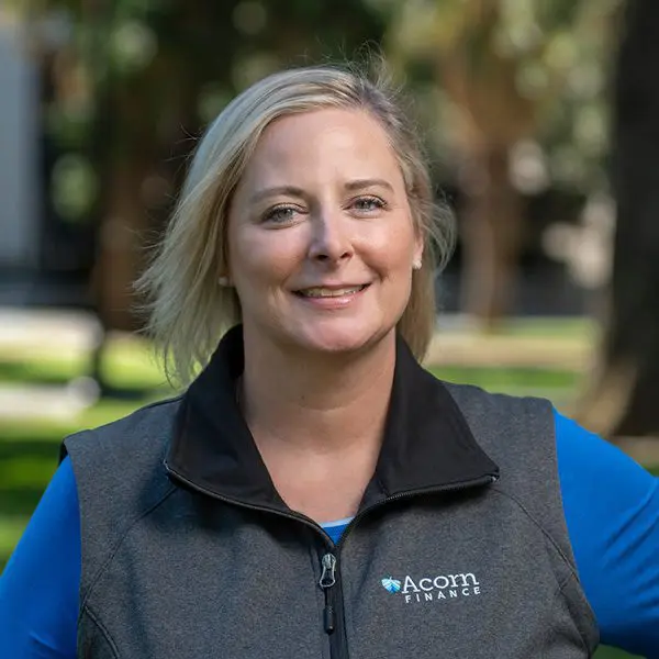 Woman in black vest with acorn finance logo smiles.
