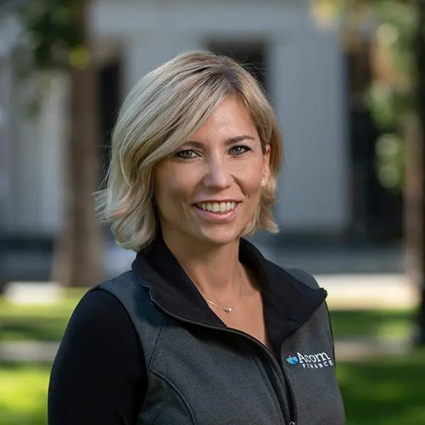 Smiling woman outside in black jacket with company logo.
