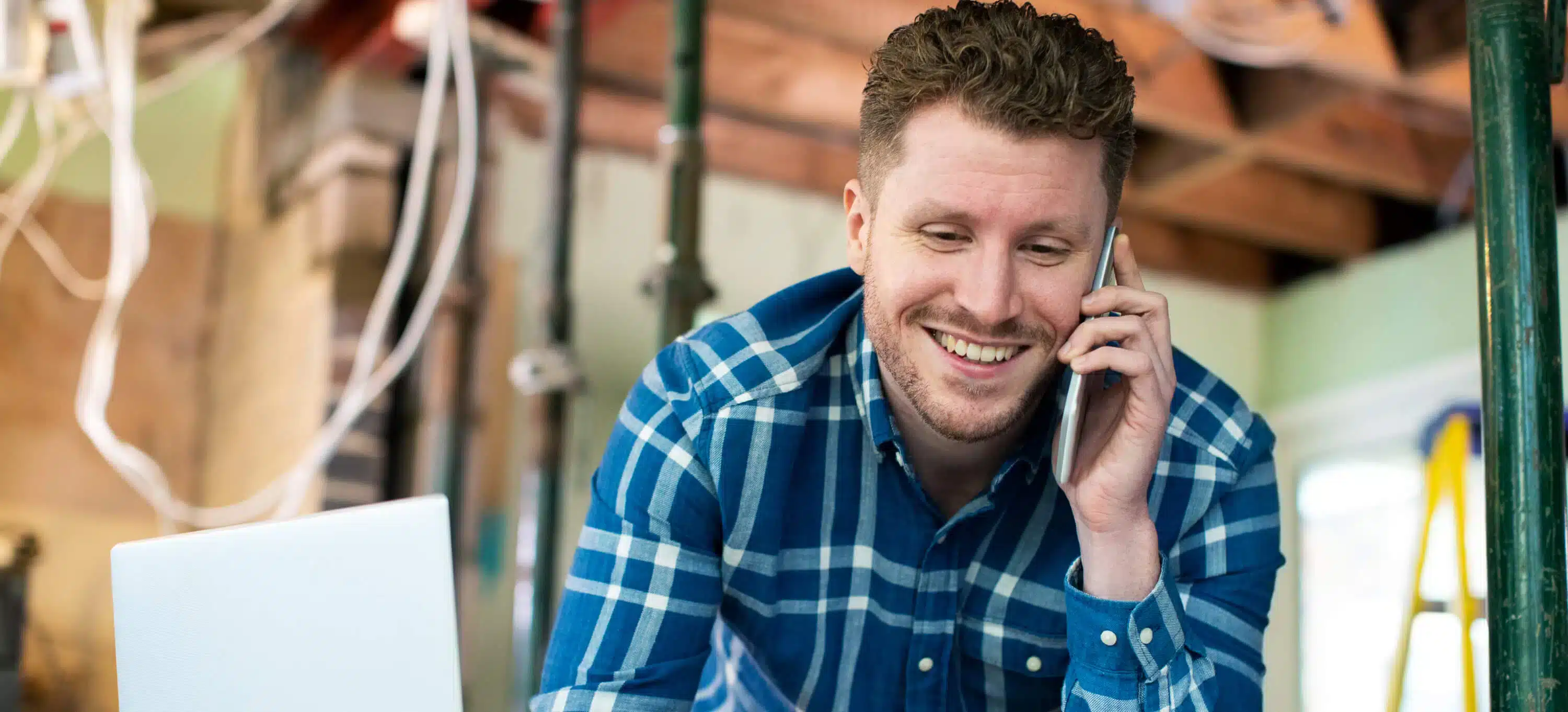 Man discusses business loan qualification on phone, smiling in workshop.