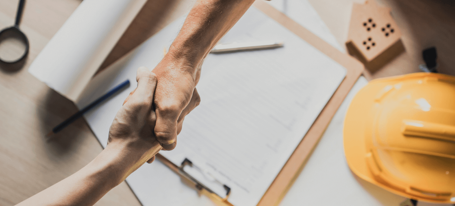 Two people handshake over table, finalizing contractor sales process.