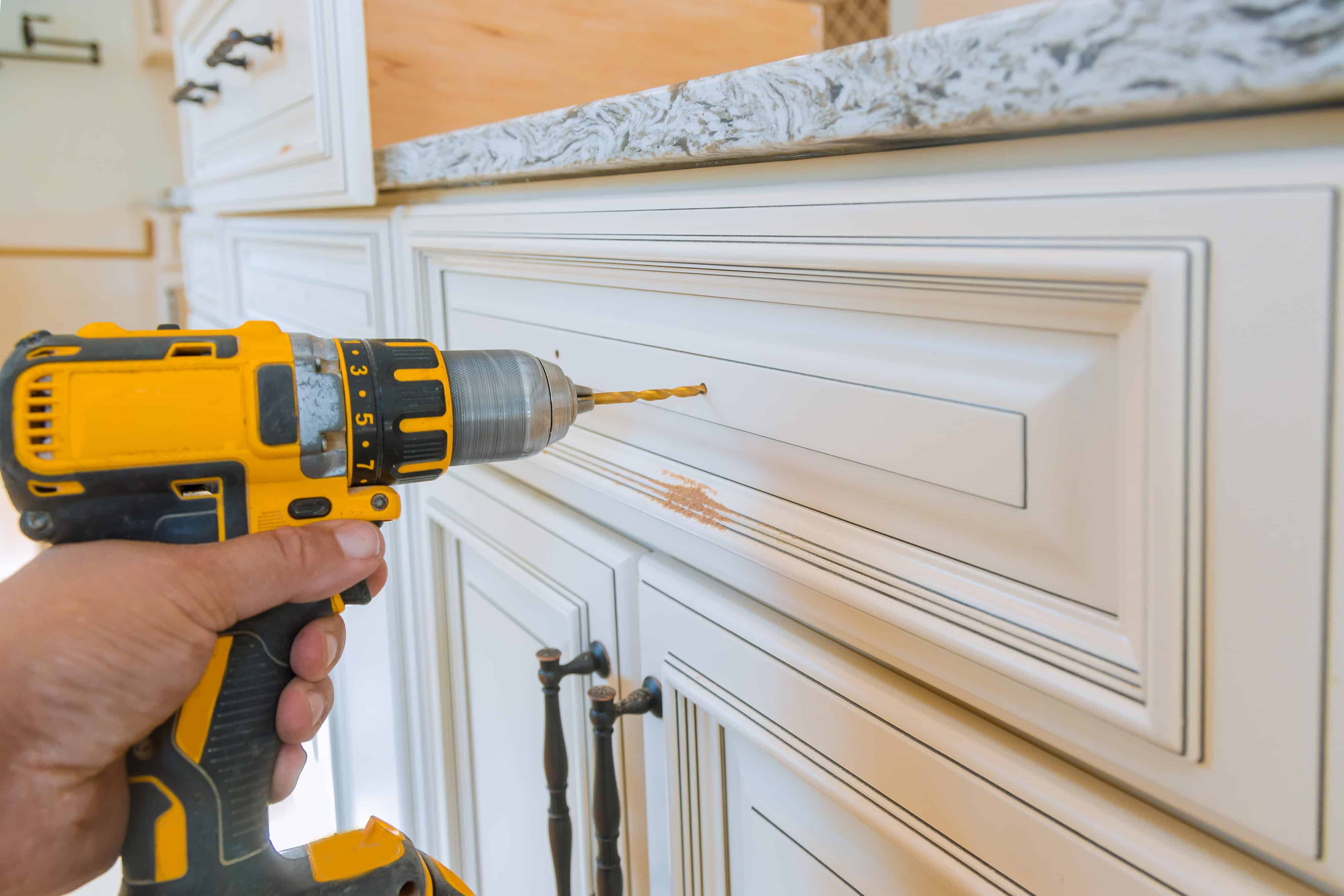 Using cordless drill to install hardware on white kitchen cabinet.