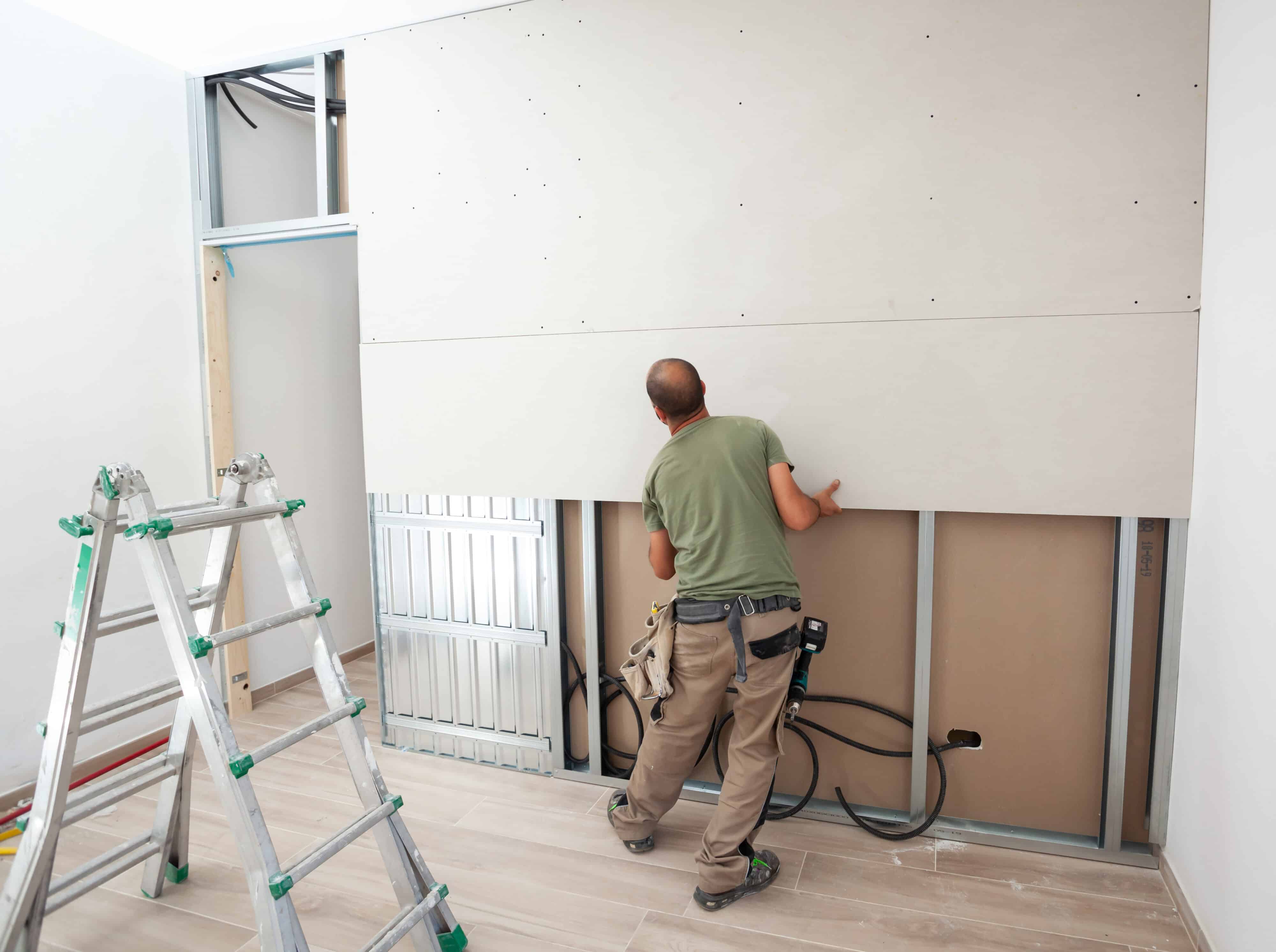 Man fitting drywall; part of basement finishing cost.